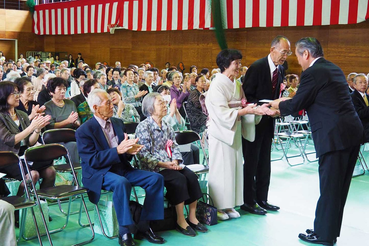 市主催の敬老会で、長寿のお年寄りに祝い金を贈る野田市長