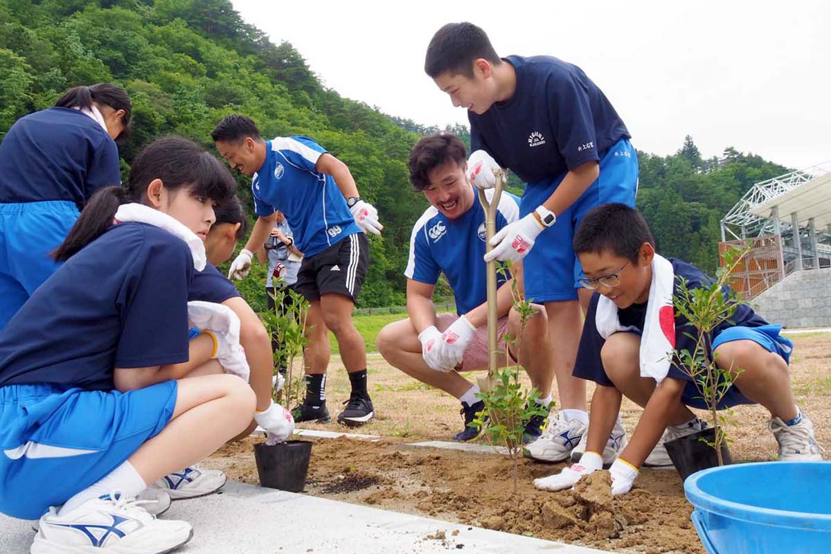 完成間近のスタジアム内にある花壇にドウダンツツジを植える釜石東中の１年生と釜石ＳＷ選手ら