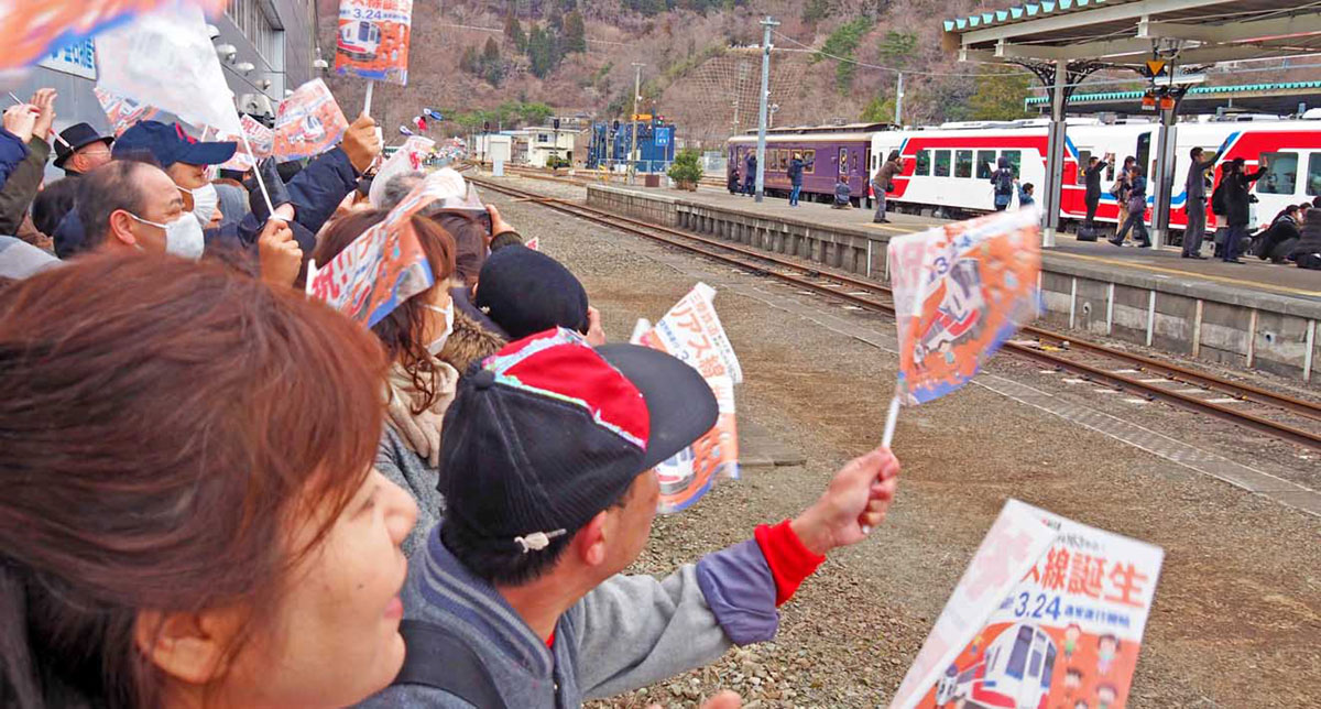 小旗を振り、記念の一番列車を見送る人たち＝２３日午前１１時４０分、釜石駅