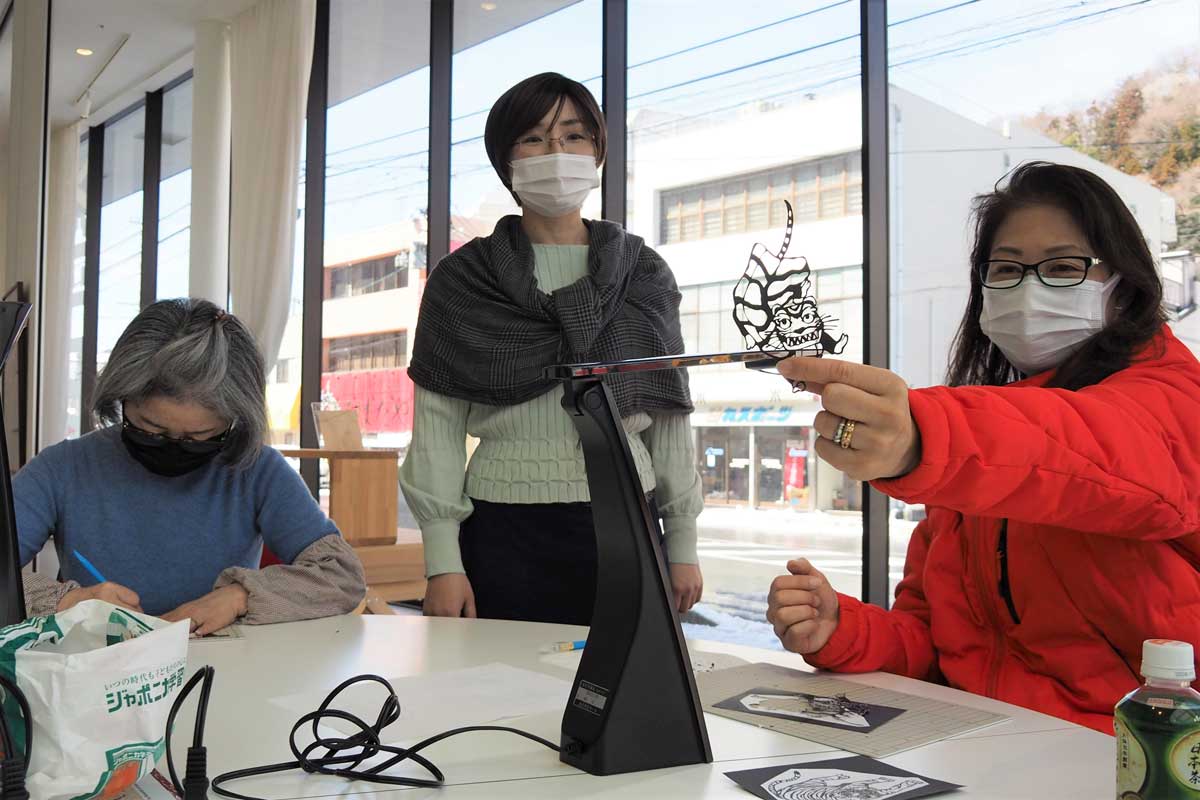 切り絵体験ワークショップで達成感を得る参加者、見守る黒須さん（中）