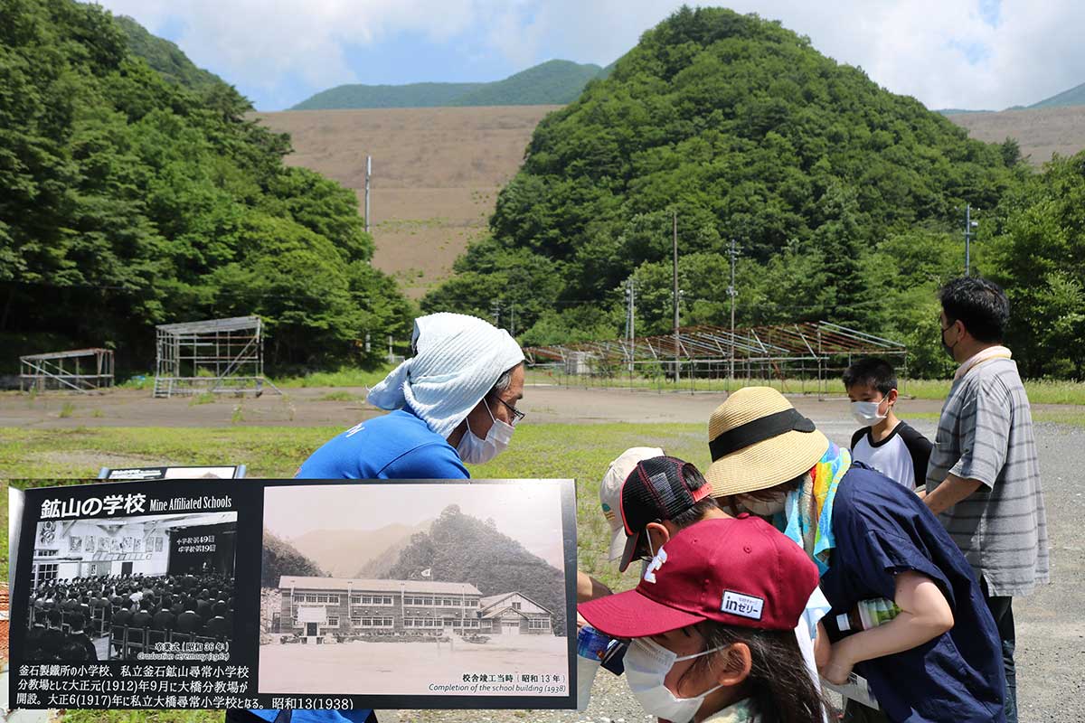 釜石鉱山学園跡地から臨む堆積場。跡地案内看板の校舎写真（左下）と比べると山の谷間を埋め立てたのが分かる