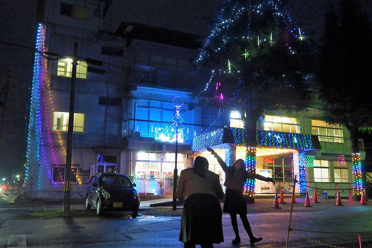 光で彩られた小佐野コミュニティ会館を背に「はい、ポーズ」