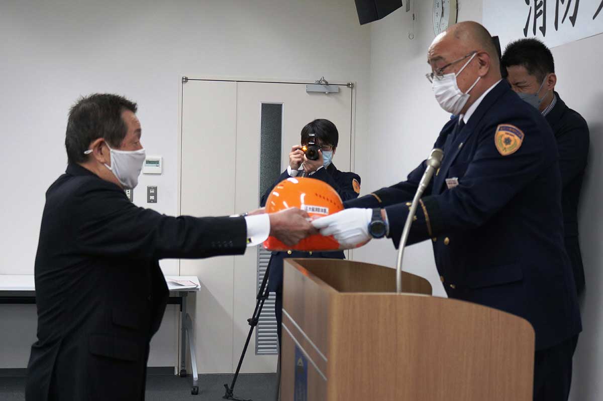登録証と活動時に着用するヘルメット、ベストなどを受け取る千葉榮さん（左）