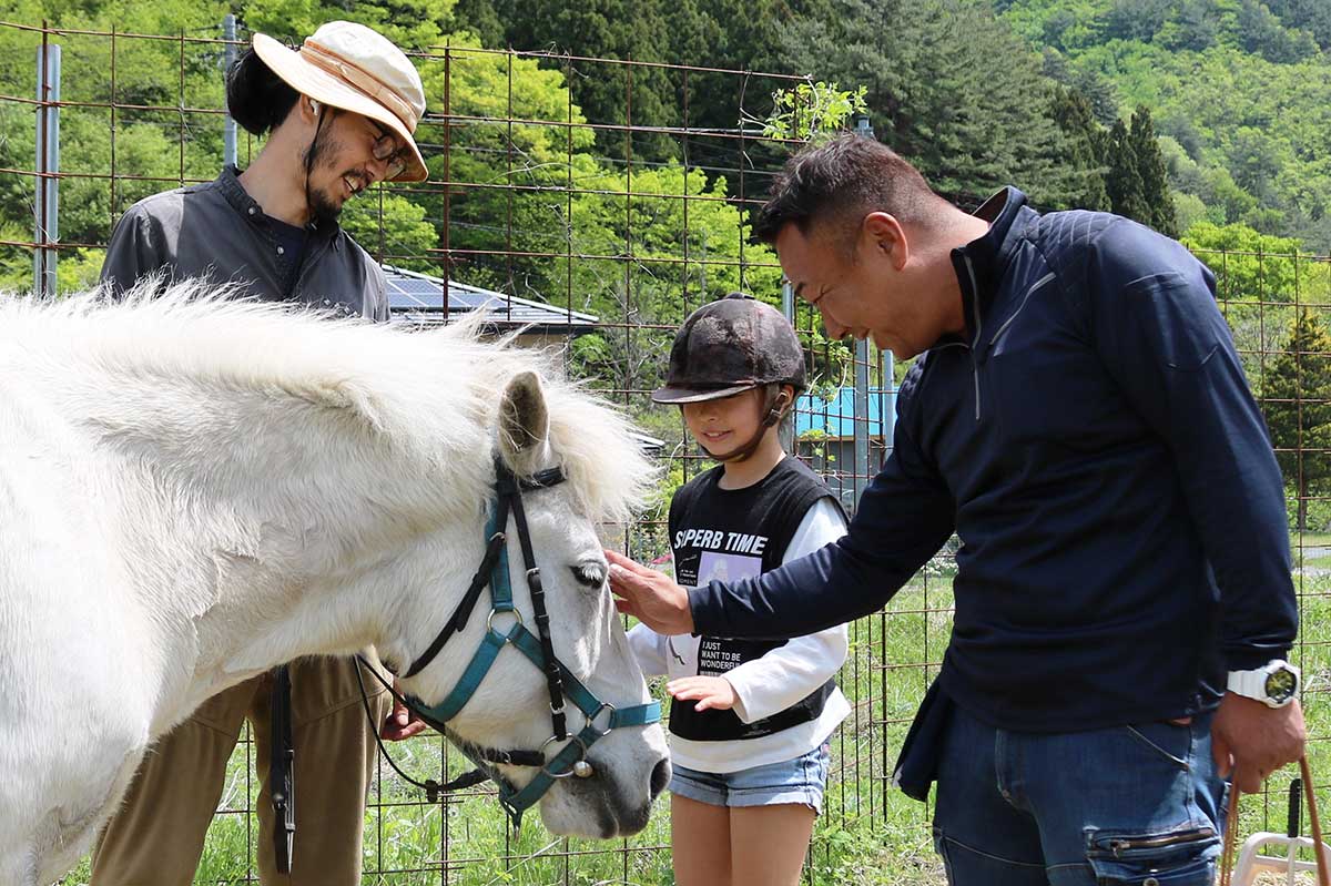 三陸駒舎の黍原豊さん（左）と話しながら、13歳馬・アサツキ（雌）と触れ合う木村さん親子