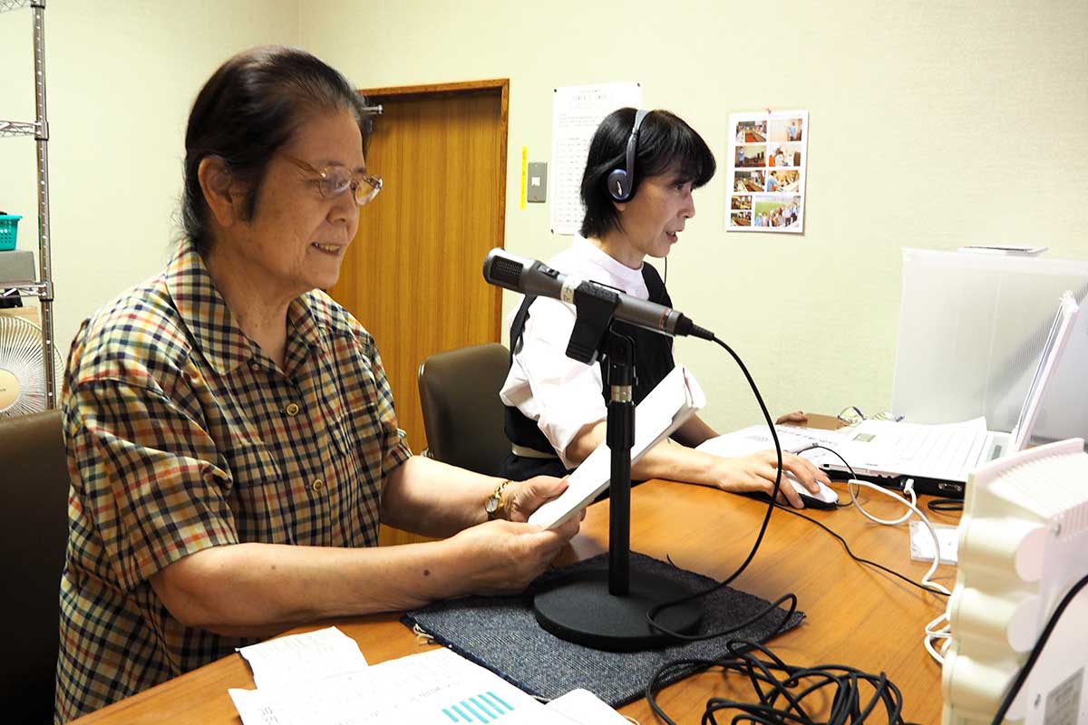 視覚障害者に届ける記事を読み、録音する松村さん（左）と藤原会長＝7月2日、釜石市立図書館