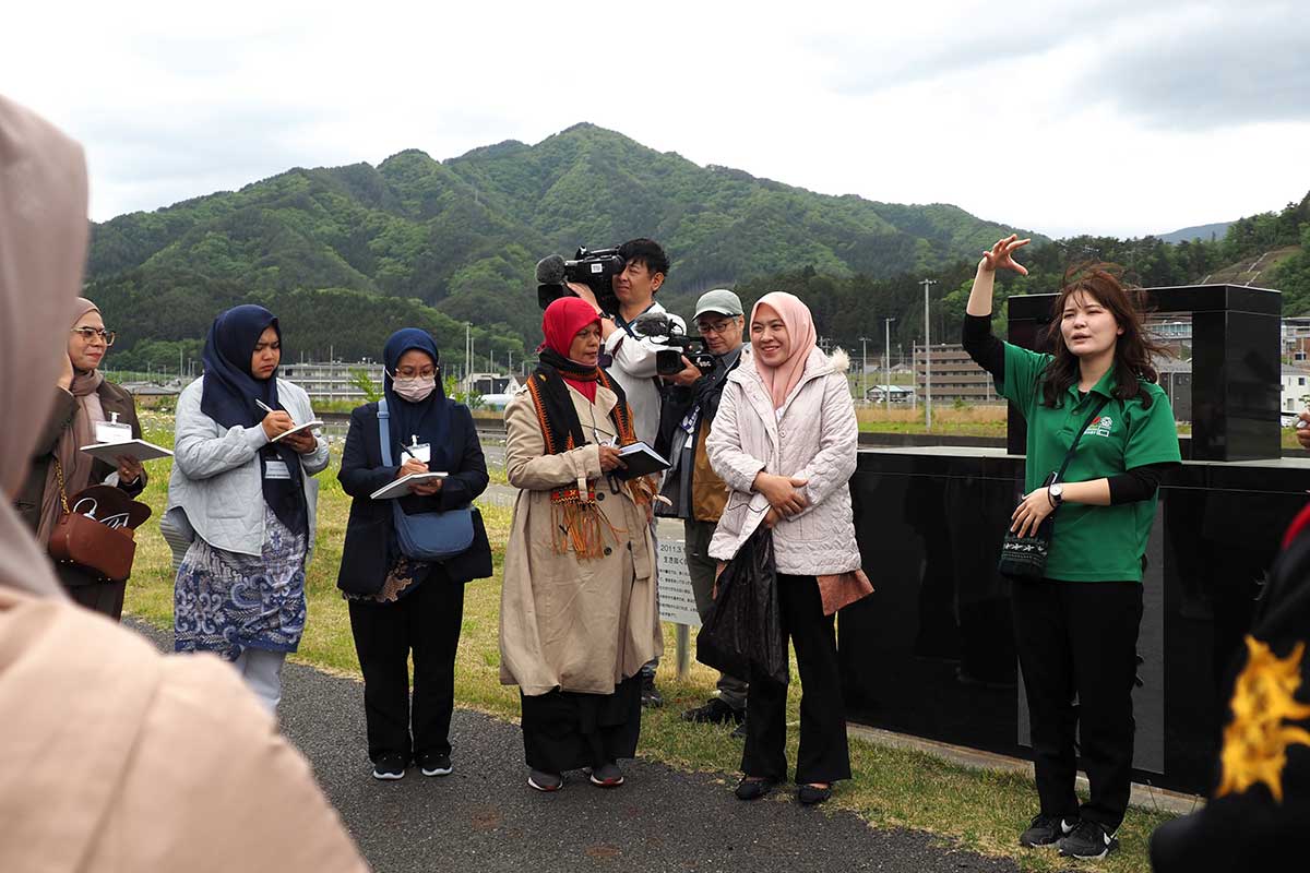 釜石鵜住居復興スタジアムの石碑の前で体験を伝える川崎杏樹さん（右）