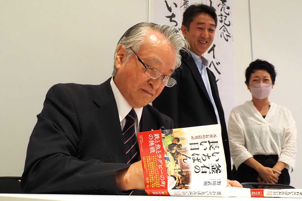 出版記念のイベントで本にサインする野田武則さん＝8月3日、釜石市民ホール