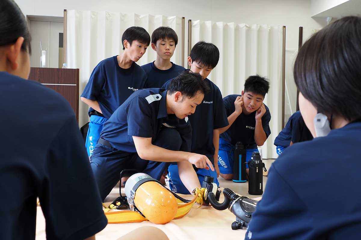 空気呼吸器の取り扱いについて説明を聞く中学生