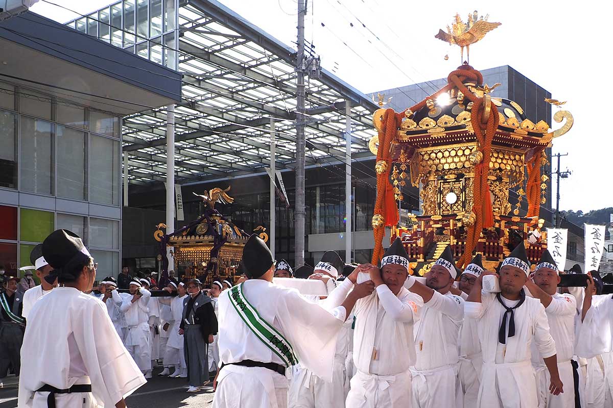 日差しを受けた2基の神輿が市街地を練り歩く＝20日