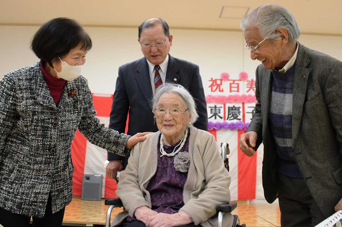 会に出席した長男直江さん（後）と義弟眞澄さん（右）、智子さん（左）夫妻から、お祝いの言葉をかけられ、ちょっぴり照れ気味の河東慶子さん