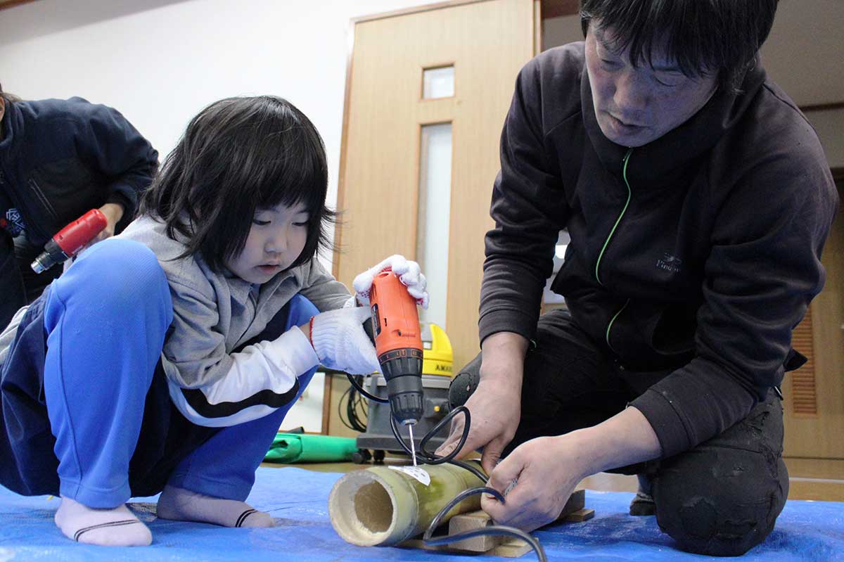 型紙の模様に合わせて電動ドリルで竹に穴を開ける児童