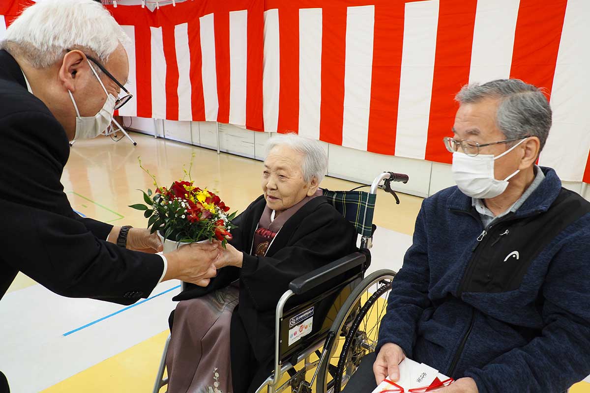 「いつまでもお元気で」。誕生祝いの花を受け取る盛さん（中）
