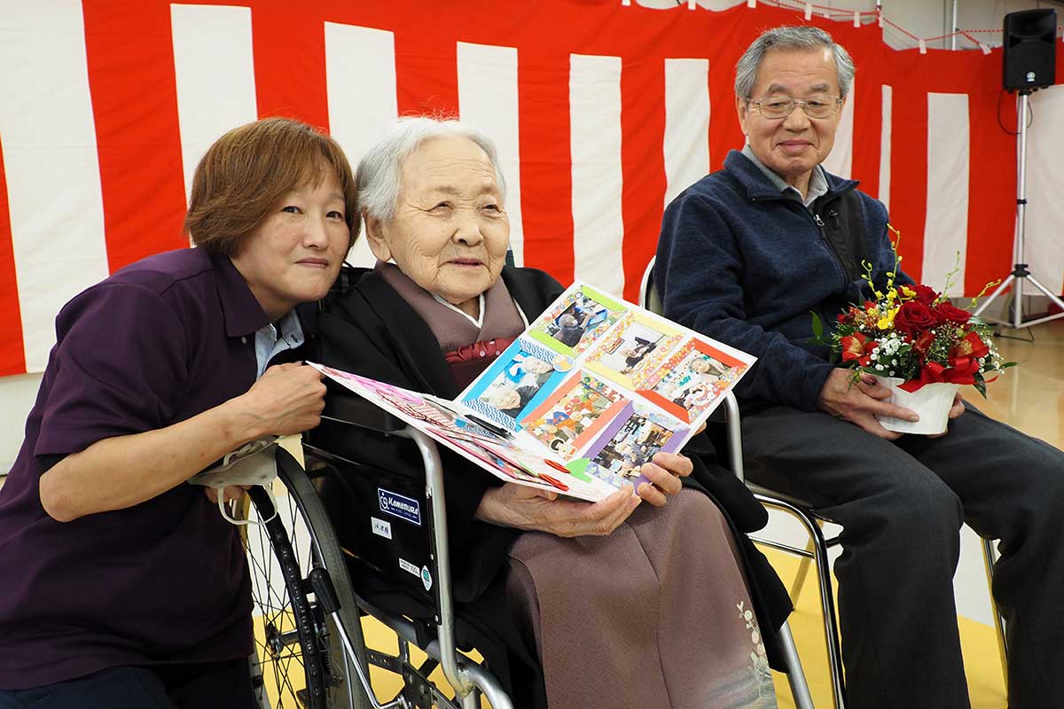 施設職員と記念にパチリ。盛さんはにこやかに笑う