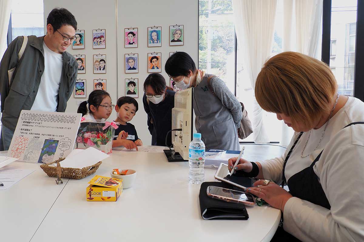 似顔絵を描く須藤さん（右）の傍らで来場者が作品を楽しむ