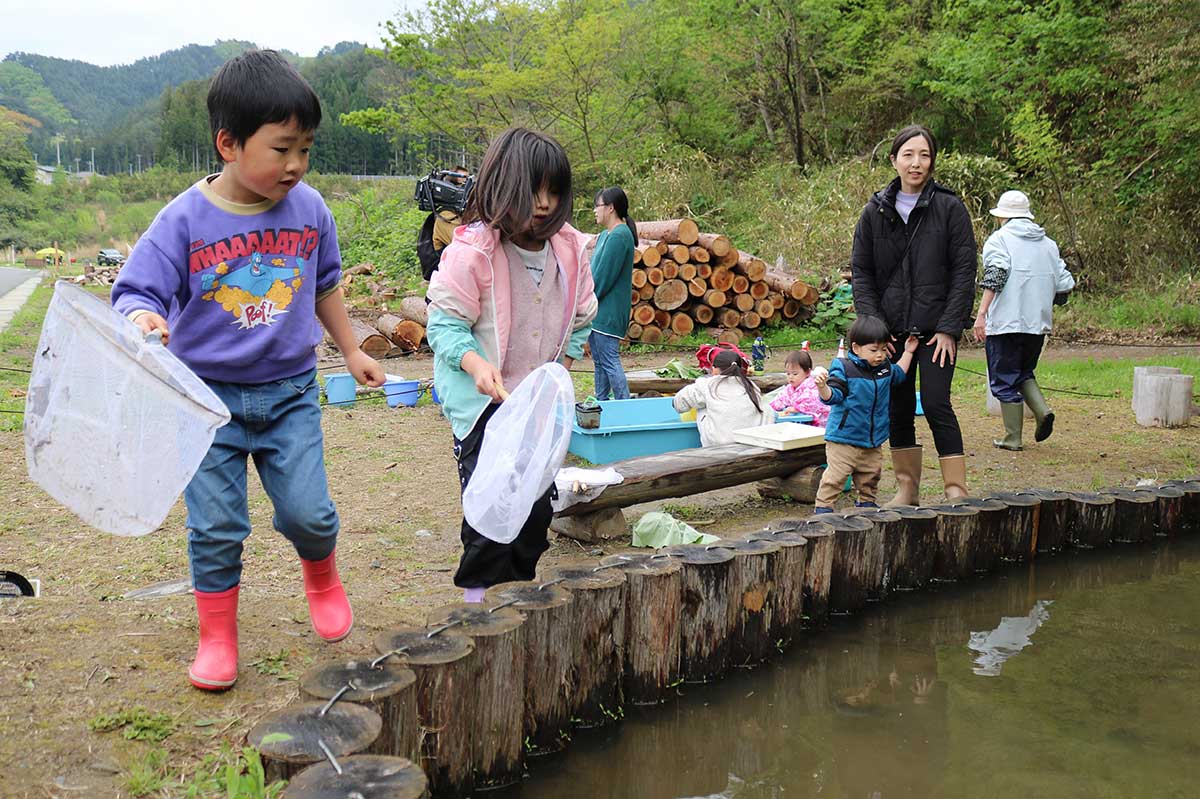 池のほとりから目を凝らし生き物を探す子どもら