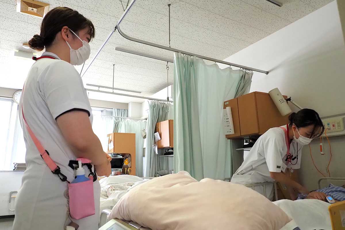 患者と向き合う佐藤さんを先輩看護師（左）が見つめる