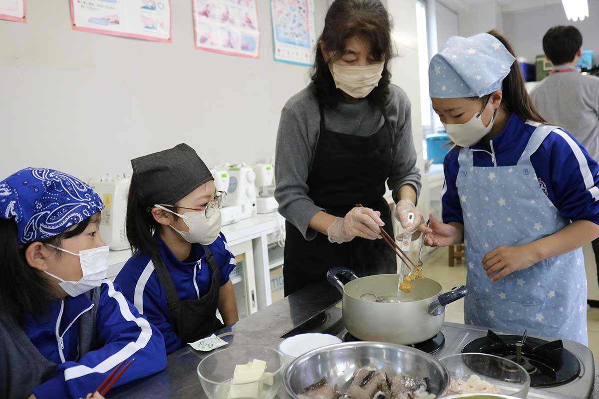 学校ボランティアの女性にサポートしてもらいながら味付け