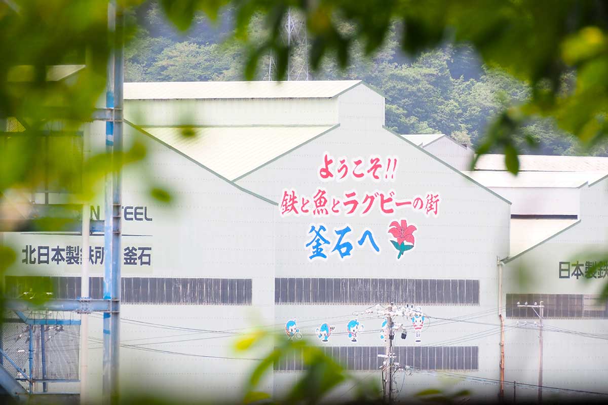 釜石小の校門前から見える製鉄所の建物とまちのキャッチコピー