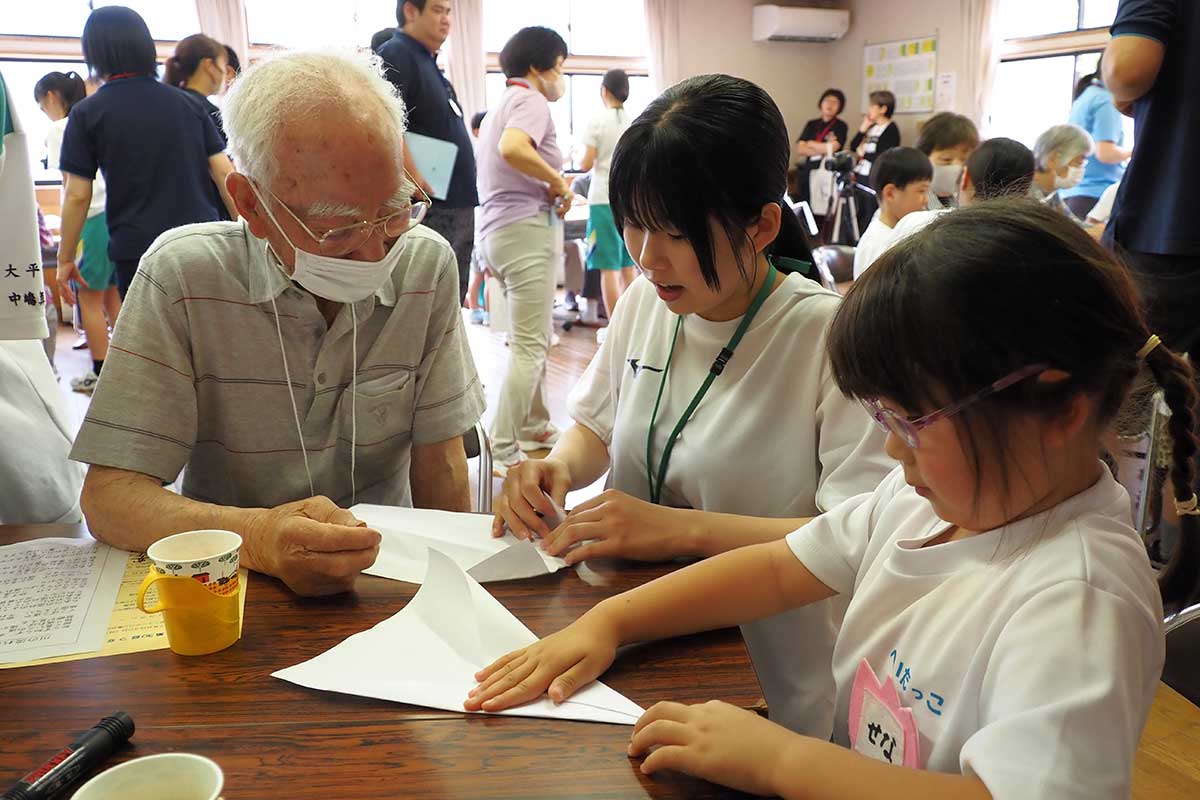 紙飛行機を作りながら地域住民や園児と交流する中学生