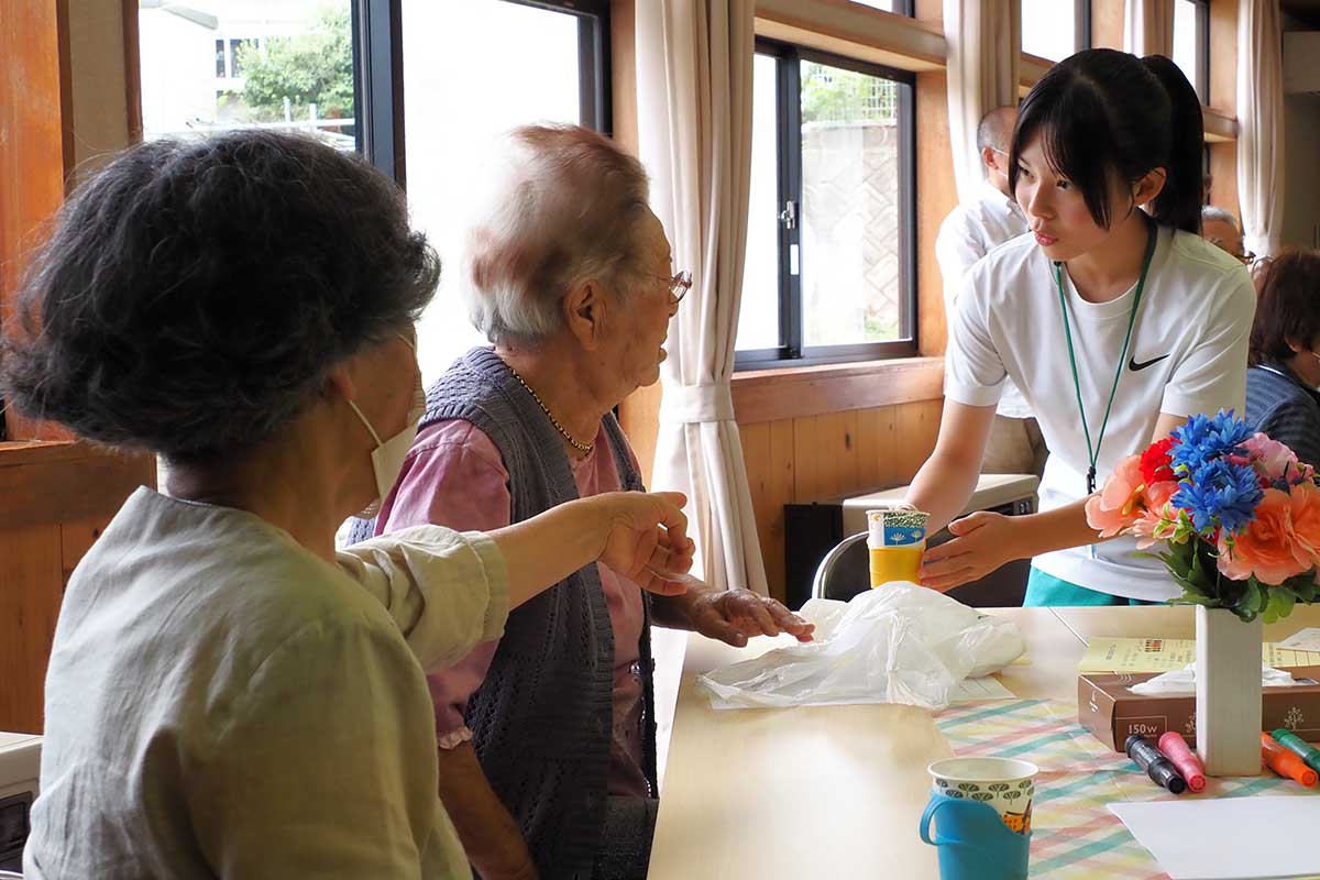 目線を合わせて笑顔で「はい、どうぞ」。学びを生かす生徒
