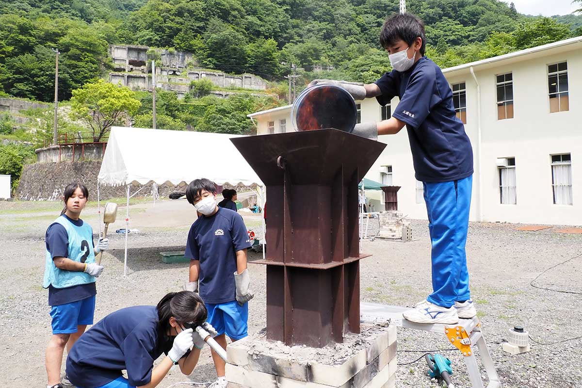 完成した炉に木炭を投入。本格的な製鉄体験に取り組む生徒＝3日