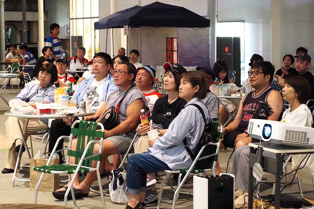 スクリーンに映し出された映像に見入るファンら