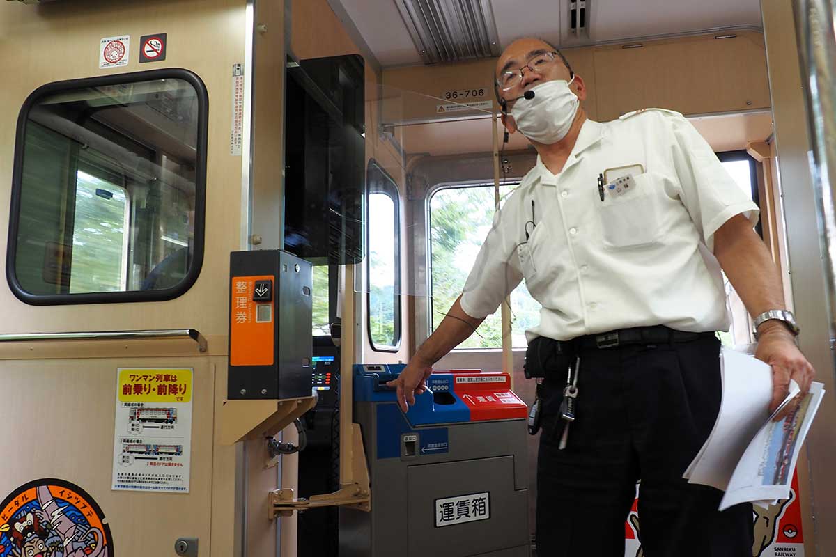 運賃箱を示して支払いの方法を伝える山蔭康明駅長