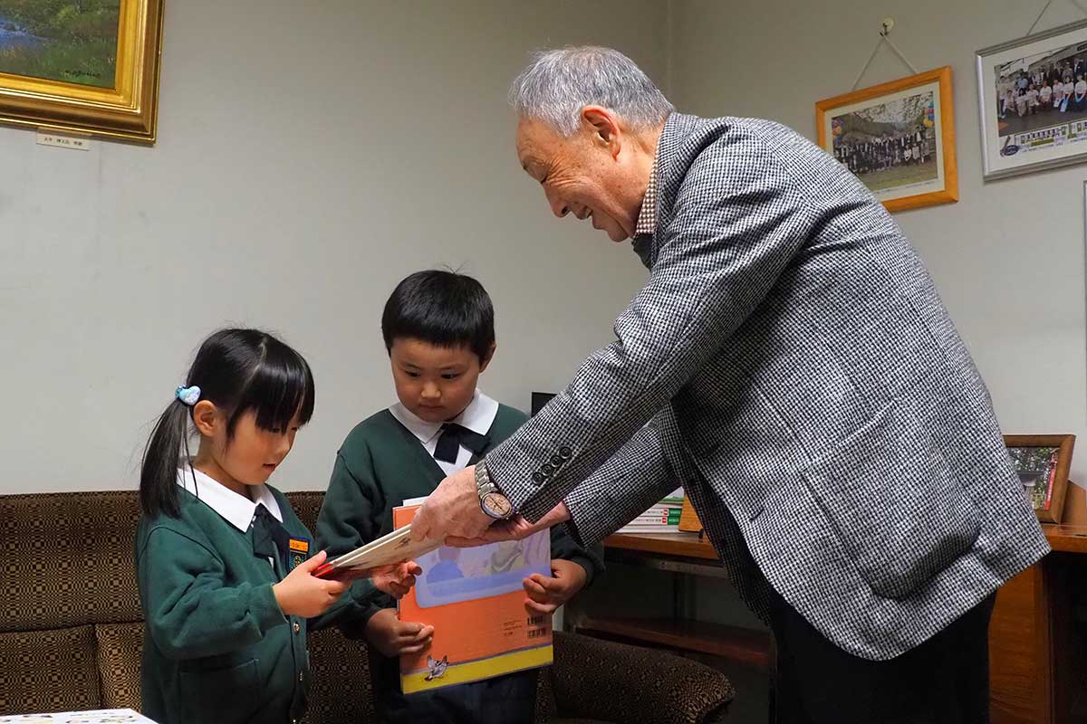 笑顔を添えながら絵本を園児に手渡す小泉会長