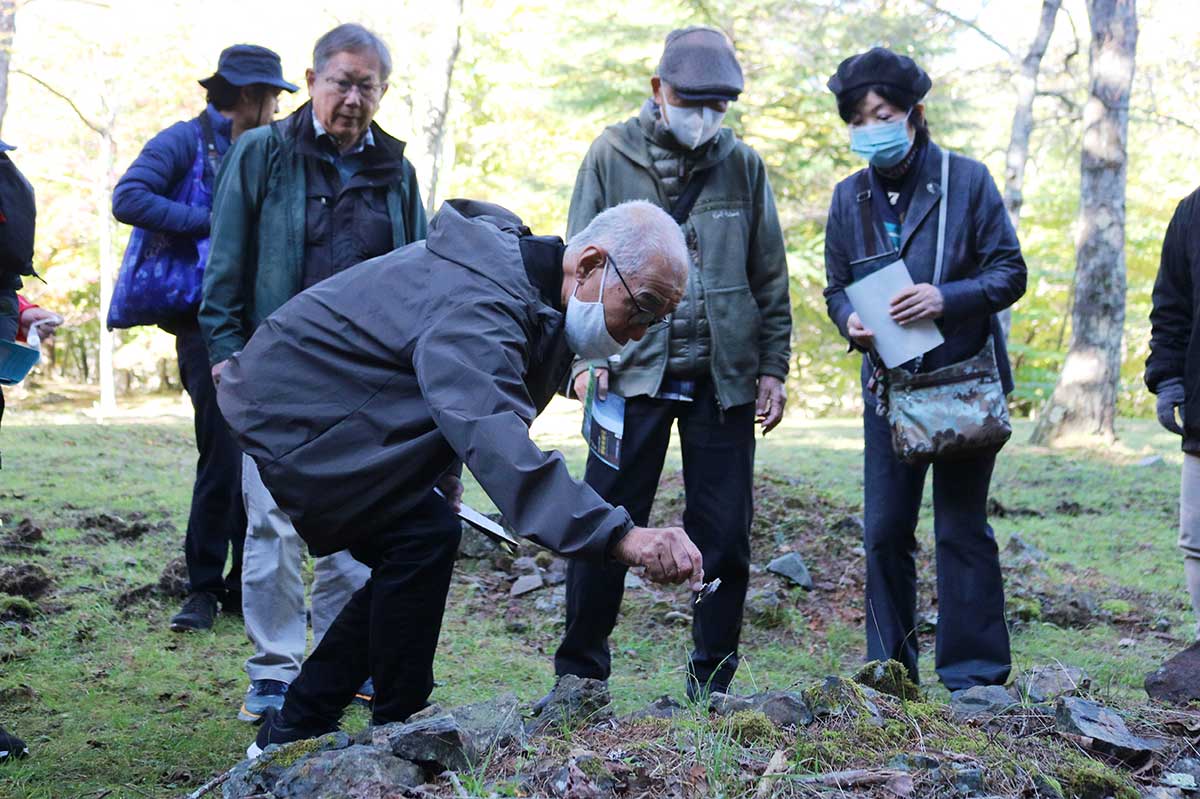 種焼場跡にある石に磁石を近づけてみる参加者。鉄鉱石が今も残る