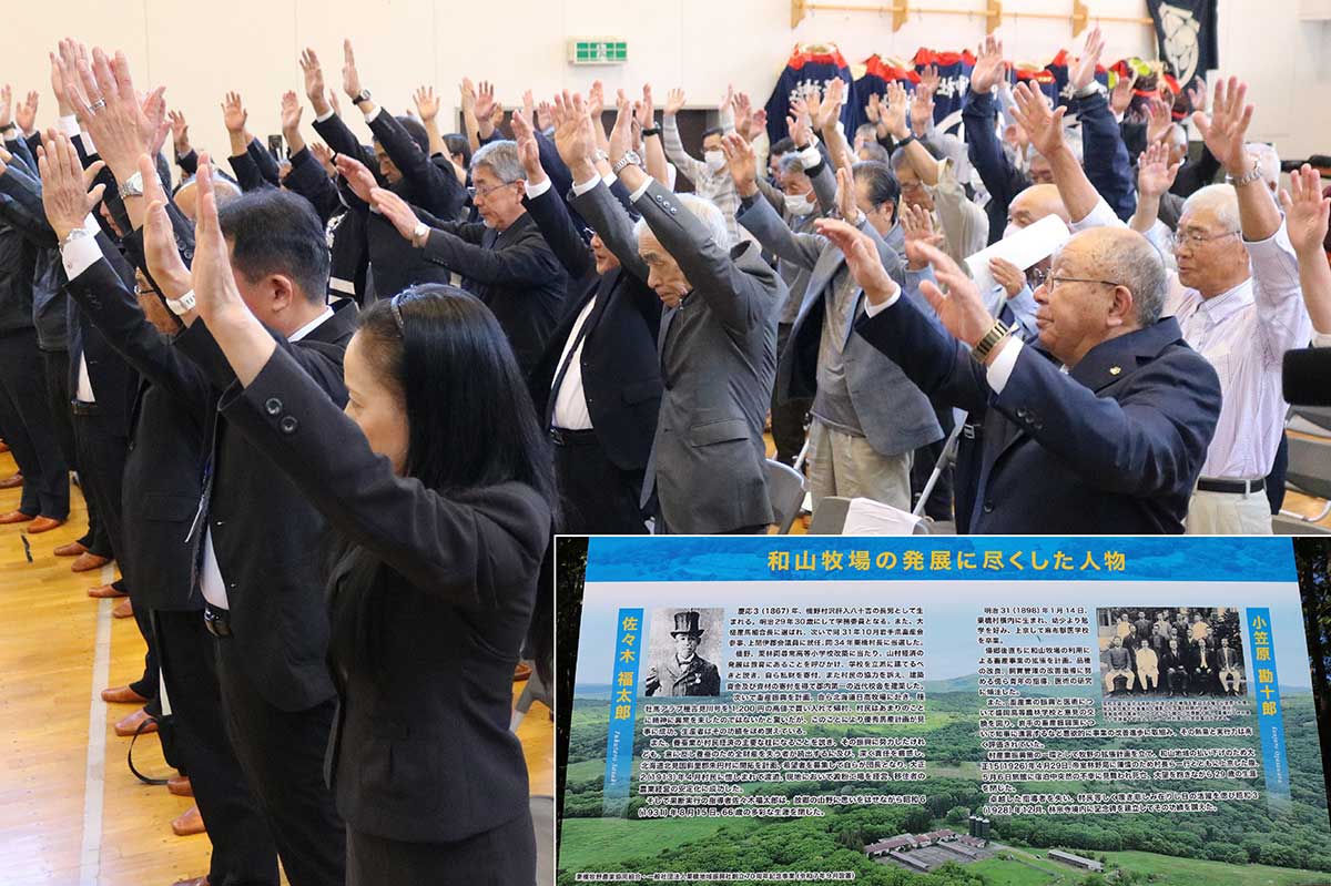 栗橋地域振興社の創立70周年記念式典で万歳三唱する出席者。記念事業で畜産業発展に貢献した先人の業績パネル（右下）を設置＝9月28日