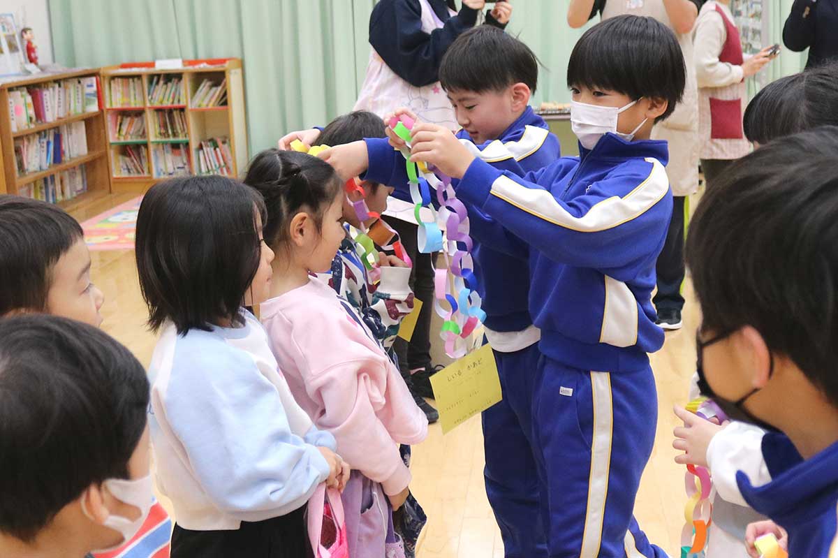 交流会の始まりにカラフルな首飾りとシールカードを園児にかけてあげる児童