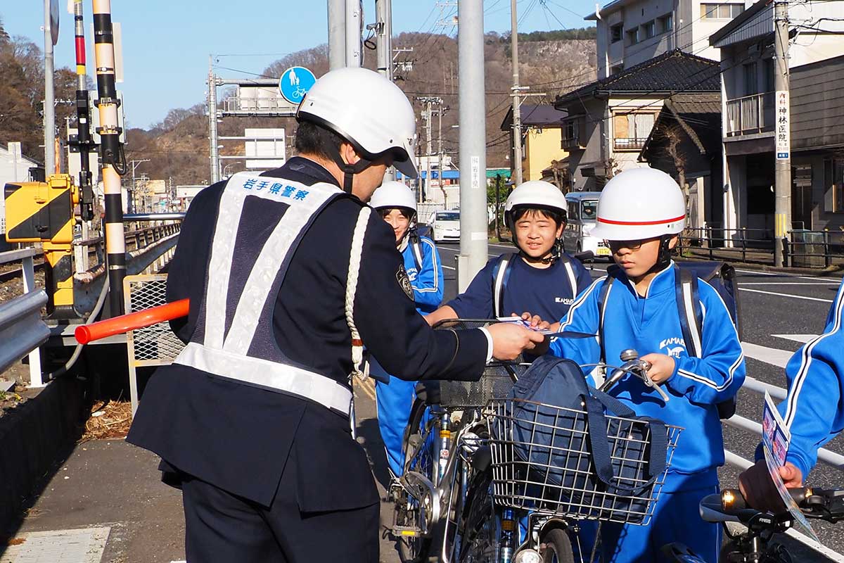 自転車通学をする中学生に啓発チラシを渡す警察官