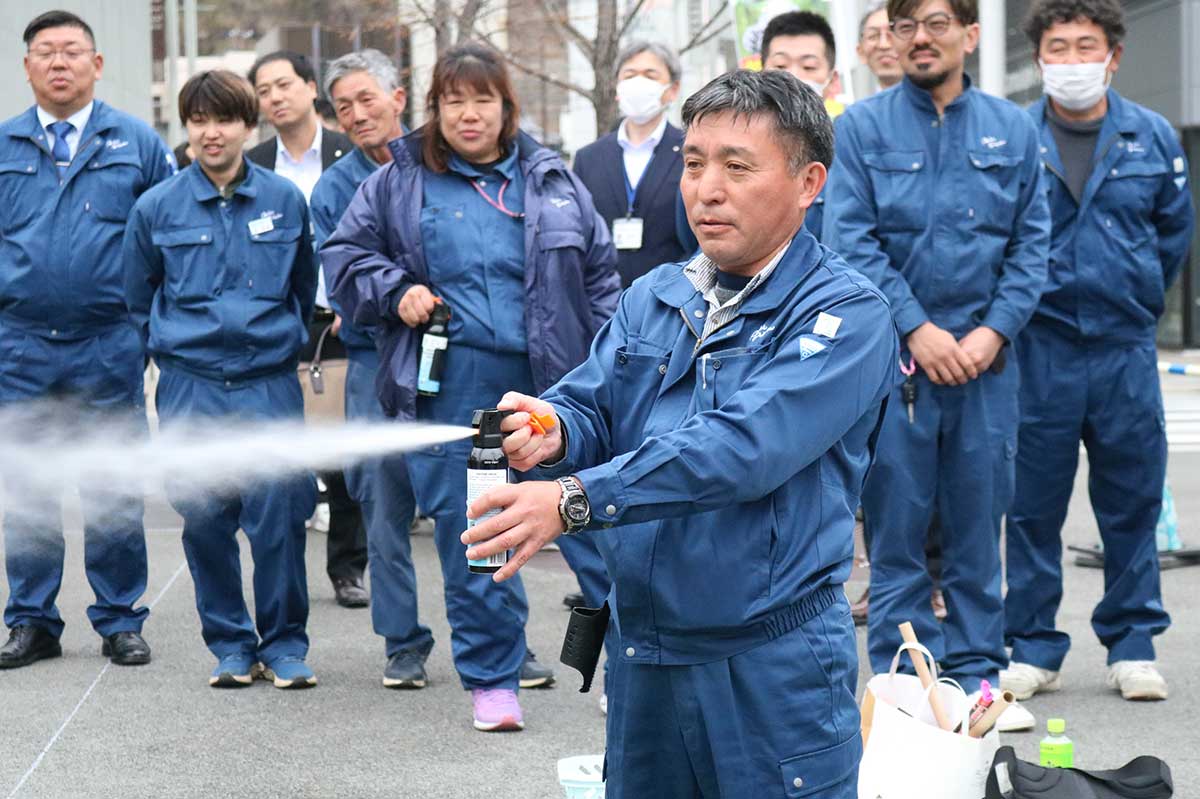 クマ撃退スプレー(練習用)の噴射を体験する青紀土木の社員=1日、大町広場