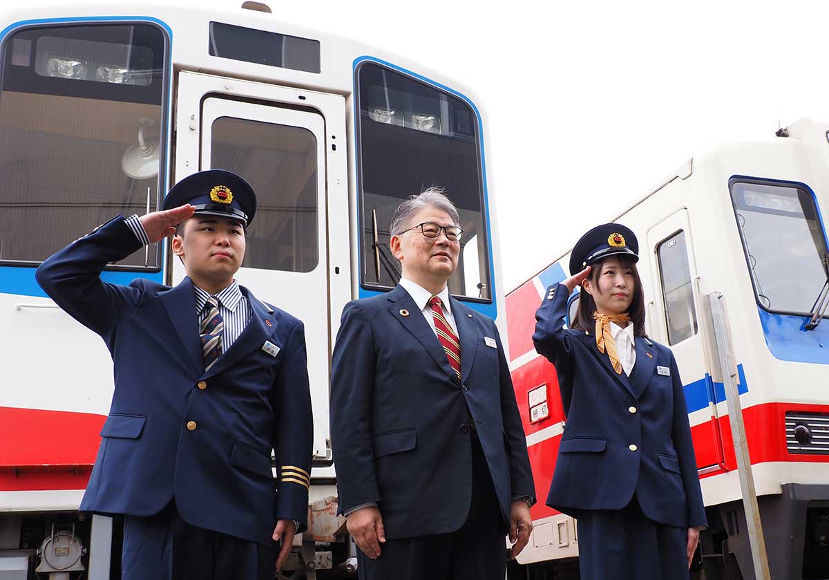 ビシッと敬礼して石川社長(中)と記念撮影する新人2人