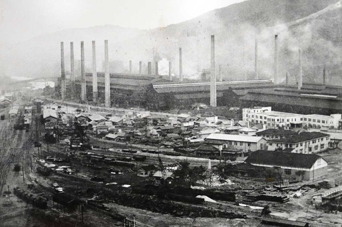 昭和25年(富士製鉄時代)の製鉄所。写真右端中央に現在も使われる本事務所(白い建物)があり、その下には附属病院の建物も見える。左端には釜石線の線路が走る