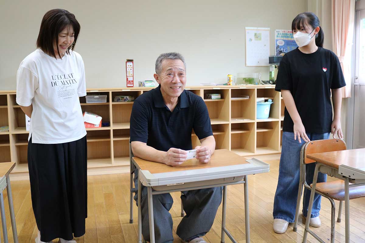教室の机と椅子に座って小学校時代の記憶をたどる卒業生 width=