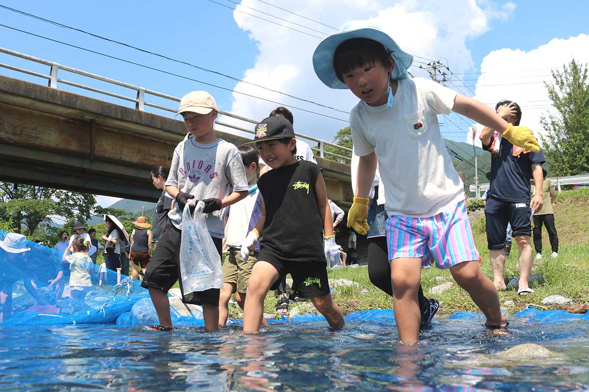 スタートの合図で特設いけすに足を踏み入れる子ども＝松倉町内会行事「魚のつかみどり」