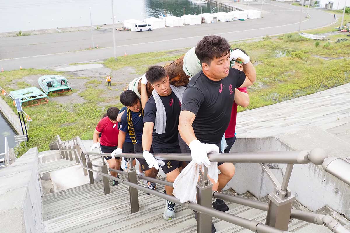 丸太を協力して運ぶ早大ラグビー部の選手たち