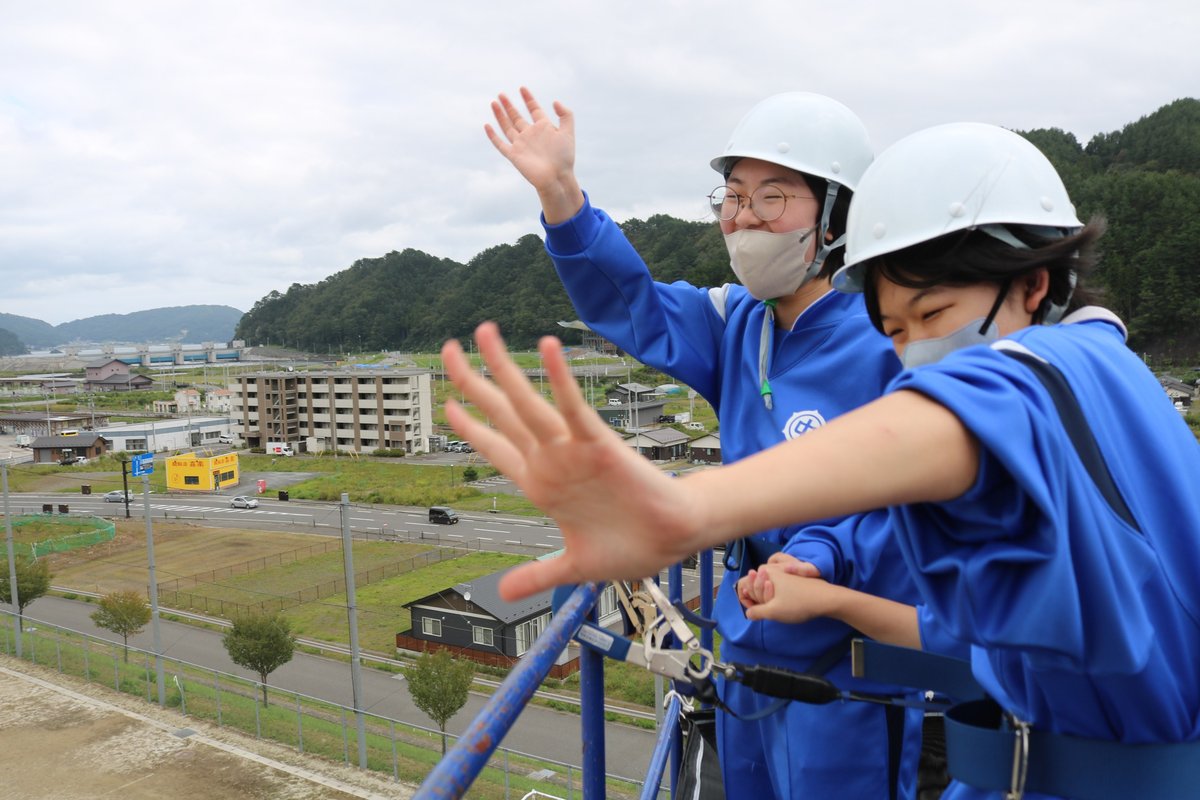 「お～い！」校庭にいる仲間に手を振る生徒。写真左中央部には鵜住居川水門、駅前の復興住宅などが見える